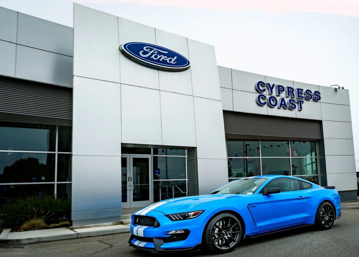 Modern Ford dealership with glass showroom and a blue Mustang parked out front